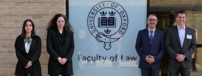 שני גברים ושתי נשים עומדים ליד סמל סגל בית הספר למשפטים של אוניברסיטת הרווארד