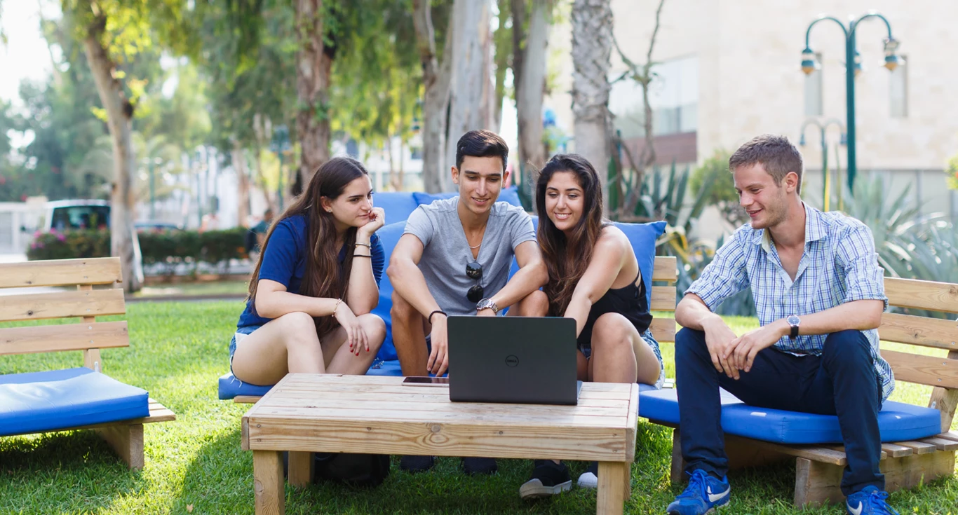 People sitting in front of a laptop on campus, on the grass