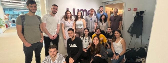 16 students posing together in front of the LUMEN company logo