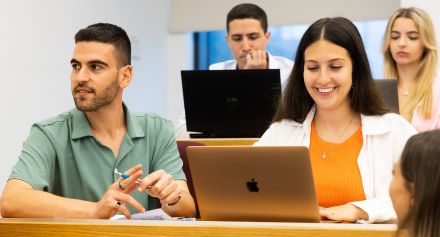 Students sitting smiling in front of laptops
