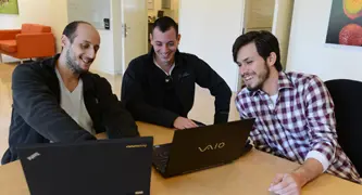 שלושה אנשים מחייכים ומדברים מול מחשב