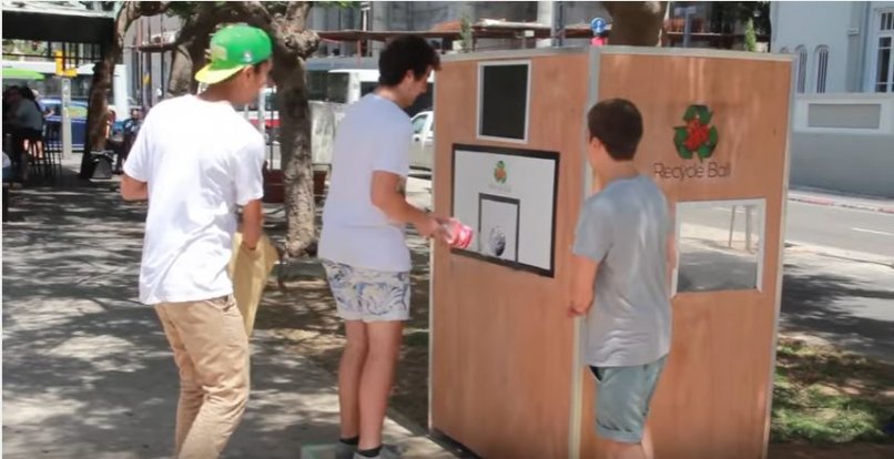 שלושה אנשים עומדים ליד פח מחזור בקבוקים